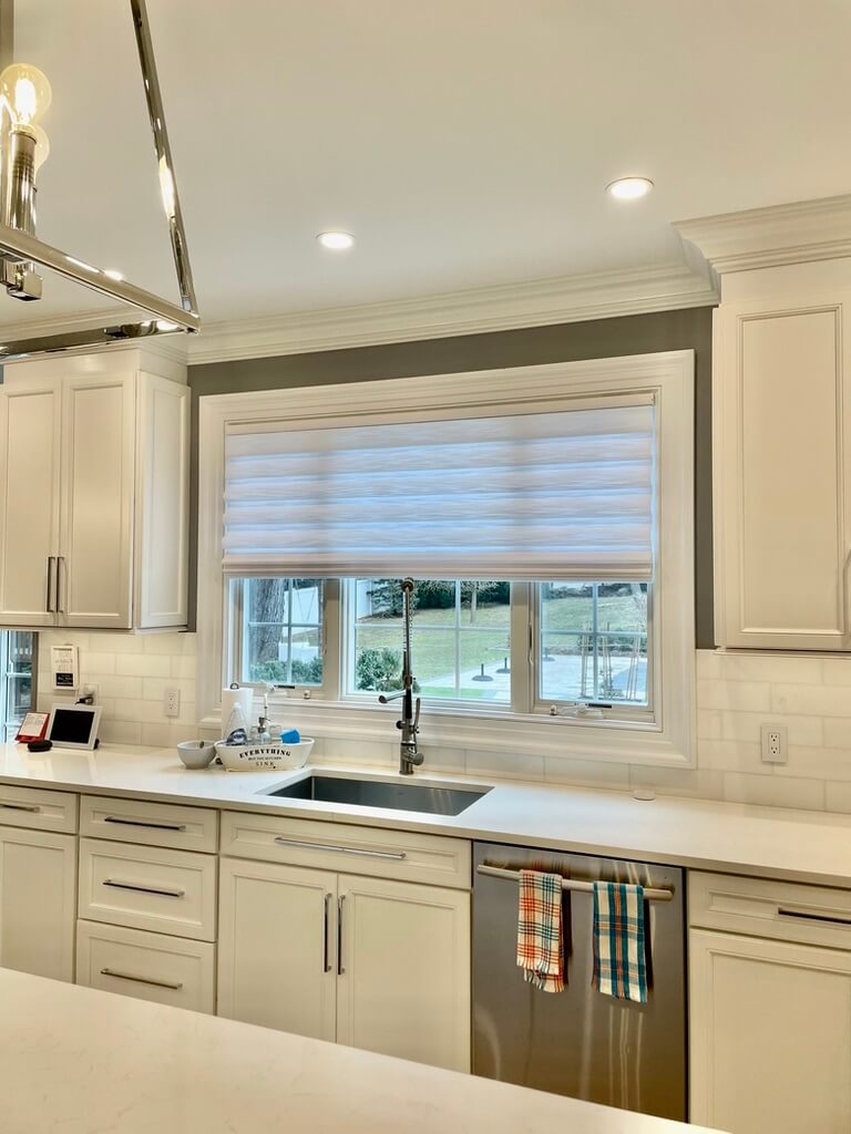 Modern Brookhaven kitchen with white cabinets and Hunter Douglas Roman shades above the sink.